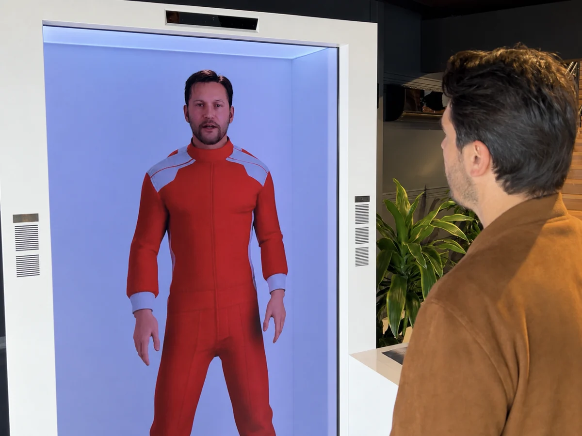 Greg, a digital host, speaking with a visitor through a transparent display at an event.