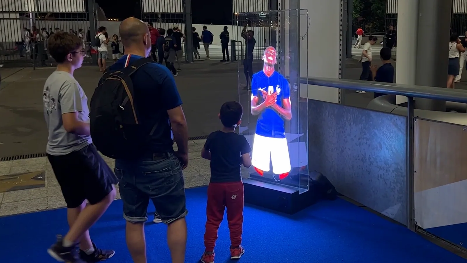 Visitors watching a life-size football character on a transparent HoloAI display outside a stadium